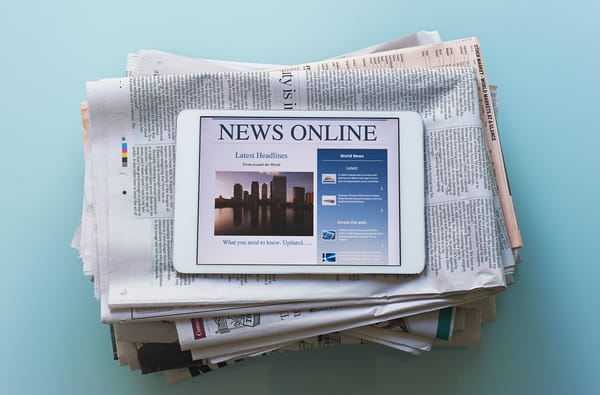 An iPad showing a news site, sitting on a stack of newspapers.
