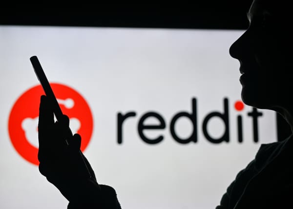 An image of a woman holding a cell phone in front of the Reddit logo displayed on a computer screen