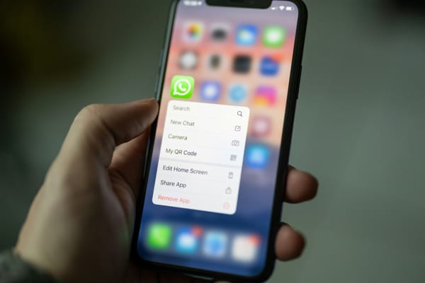A hand holding an iPhone with WhatsApp highlighted and its context menu open