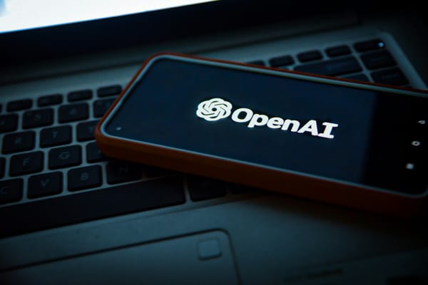 OpenAI logo displayed on a black smartphone angled on top of a black laptop keyboard