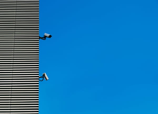 Surveillance cameras on the side of a building next to a blue sky
