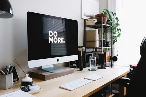 An angled photo of an iMac showing the words DO MORE. on a black screen in a home office