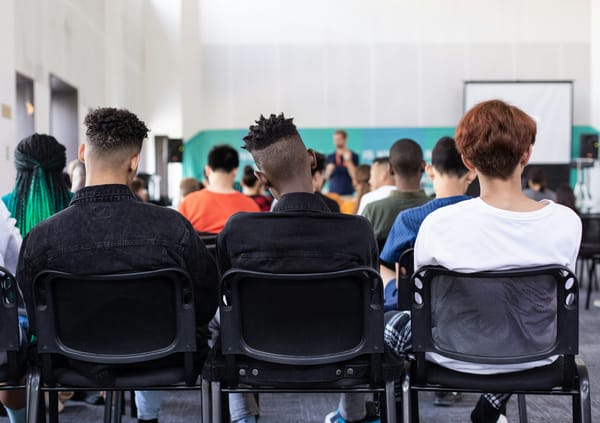 Photo of a classroom taken from the rear of the room, with more than a dozen students shown from the back facing their teacher