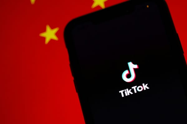 The TikTok app splash screen on a phone held against a Chinese flag in the background