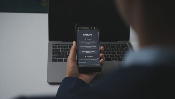 ChatGPT shown open on a smartphone held against the backdrop of a MacBook