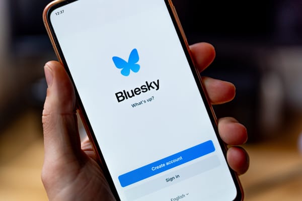 The Bluesky login screen shown on an iPhone in a person's hand 
